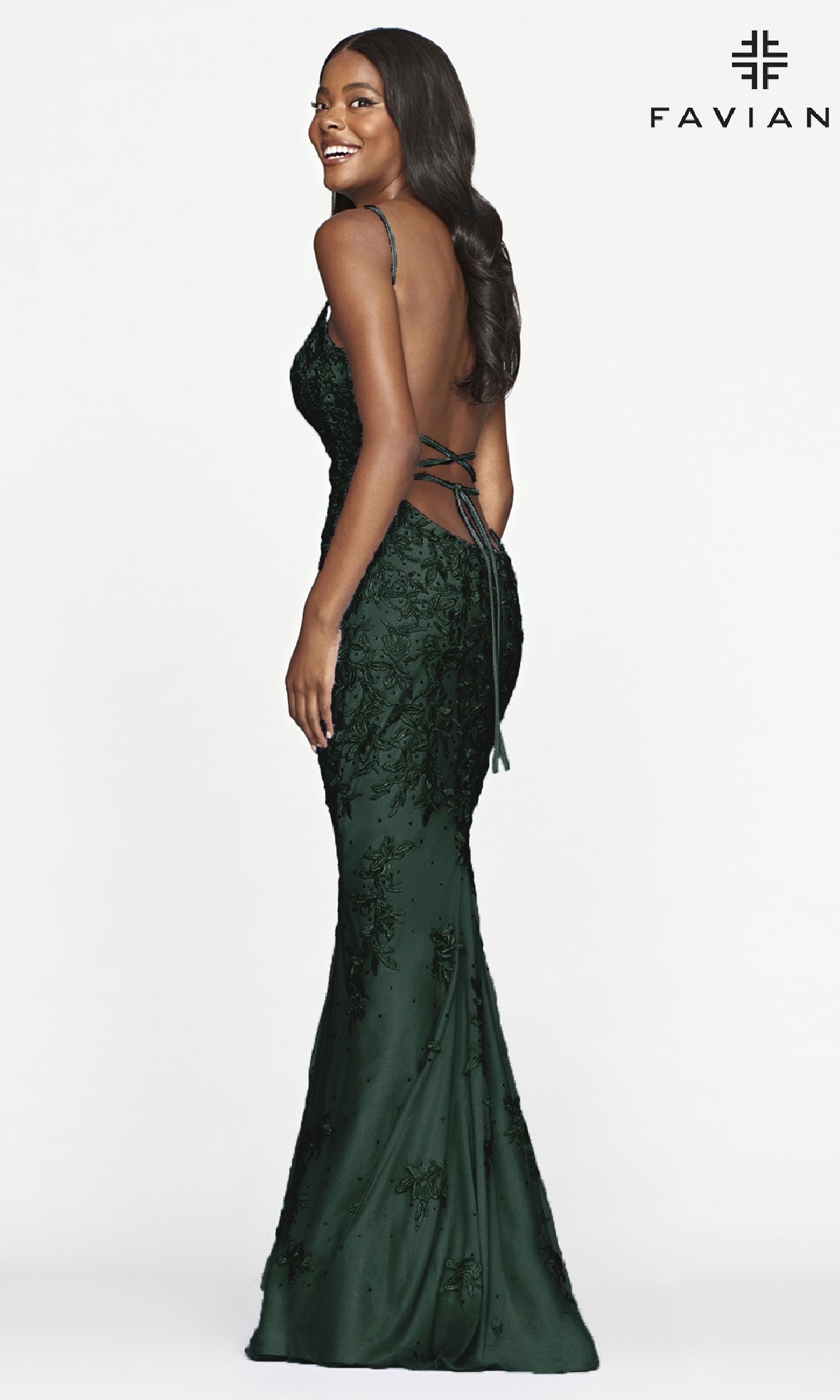 Woman in a dark green Faviana Lace Embroidery Long Backless Prom Dress stands sideways, smiling. The fitted gown has thin straps and lace embroidery.